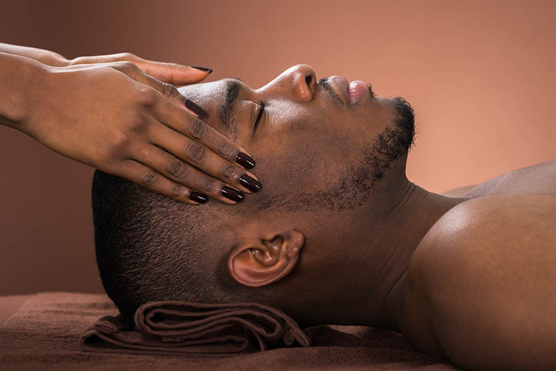 Young African Man Receiving Forehead Massage In Spa